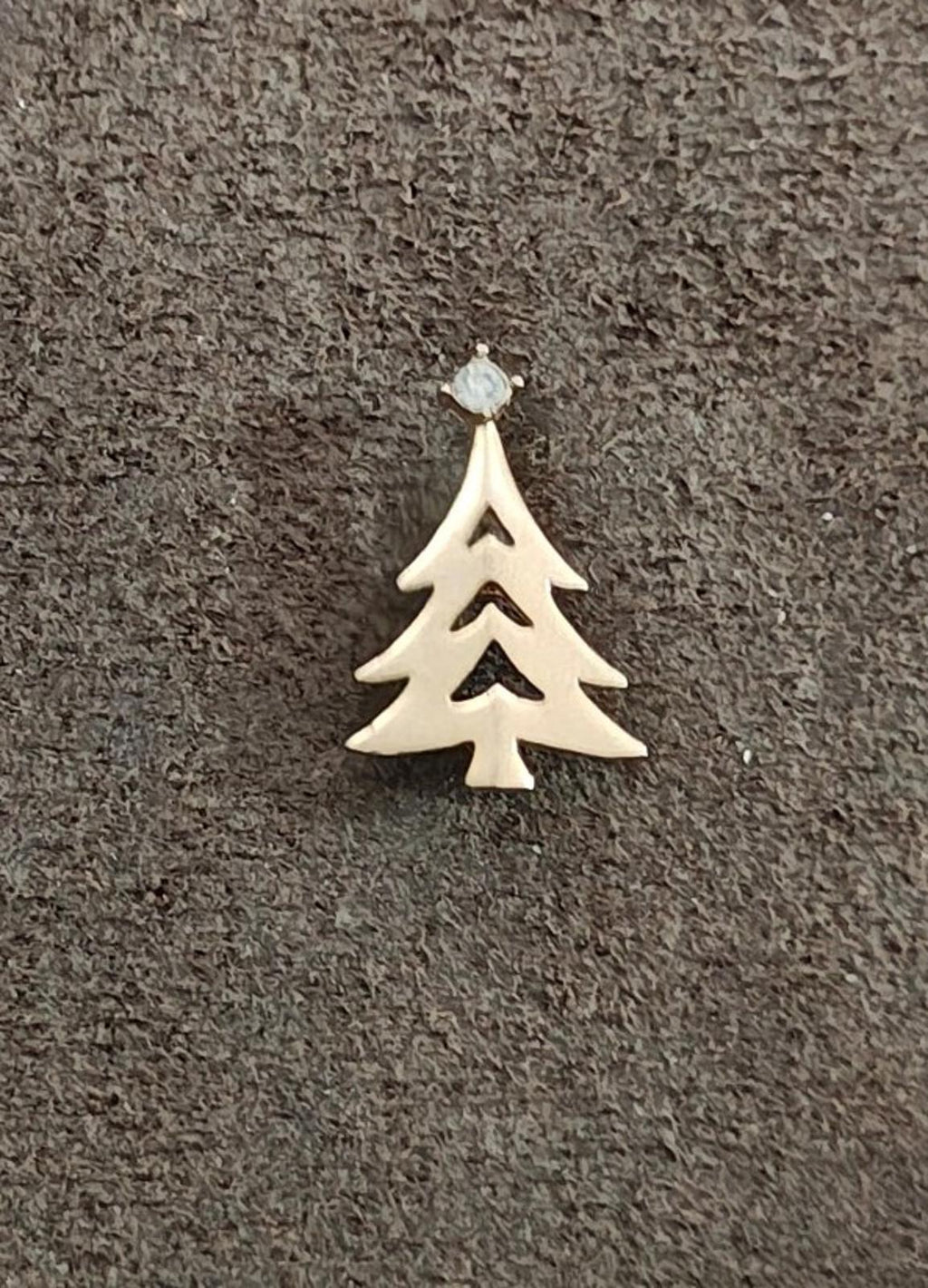 Gold-tone Christmas tree charm with clear rhinestone top on textured surface