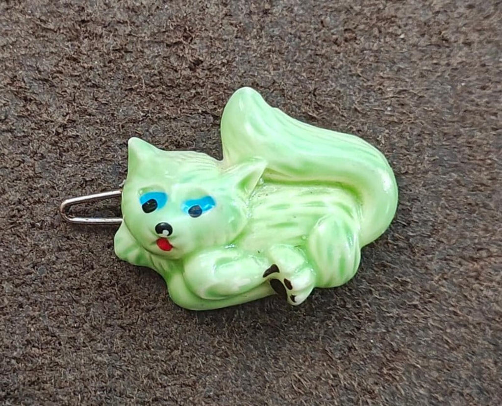 Green cat-shaped hard plastic barrette with blue eyes and metal clasp pin