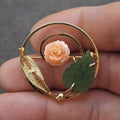 Gold-tone filigree brooch with pale rose cabochon and green leaf accents.