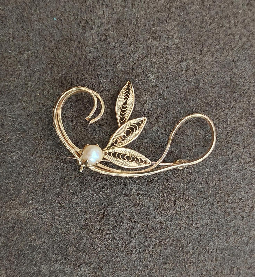 Gold tone leaf filigree brooch with faux pearl bead, leaf cutout detail, angled view