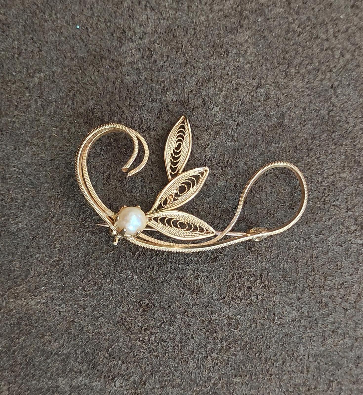 Gold tone leaf filigree brooch with faux pearl bead, leaf cutout detail, angled view