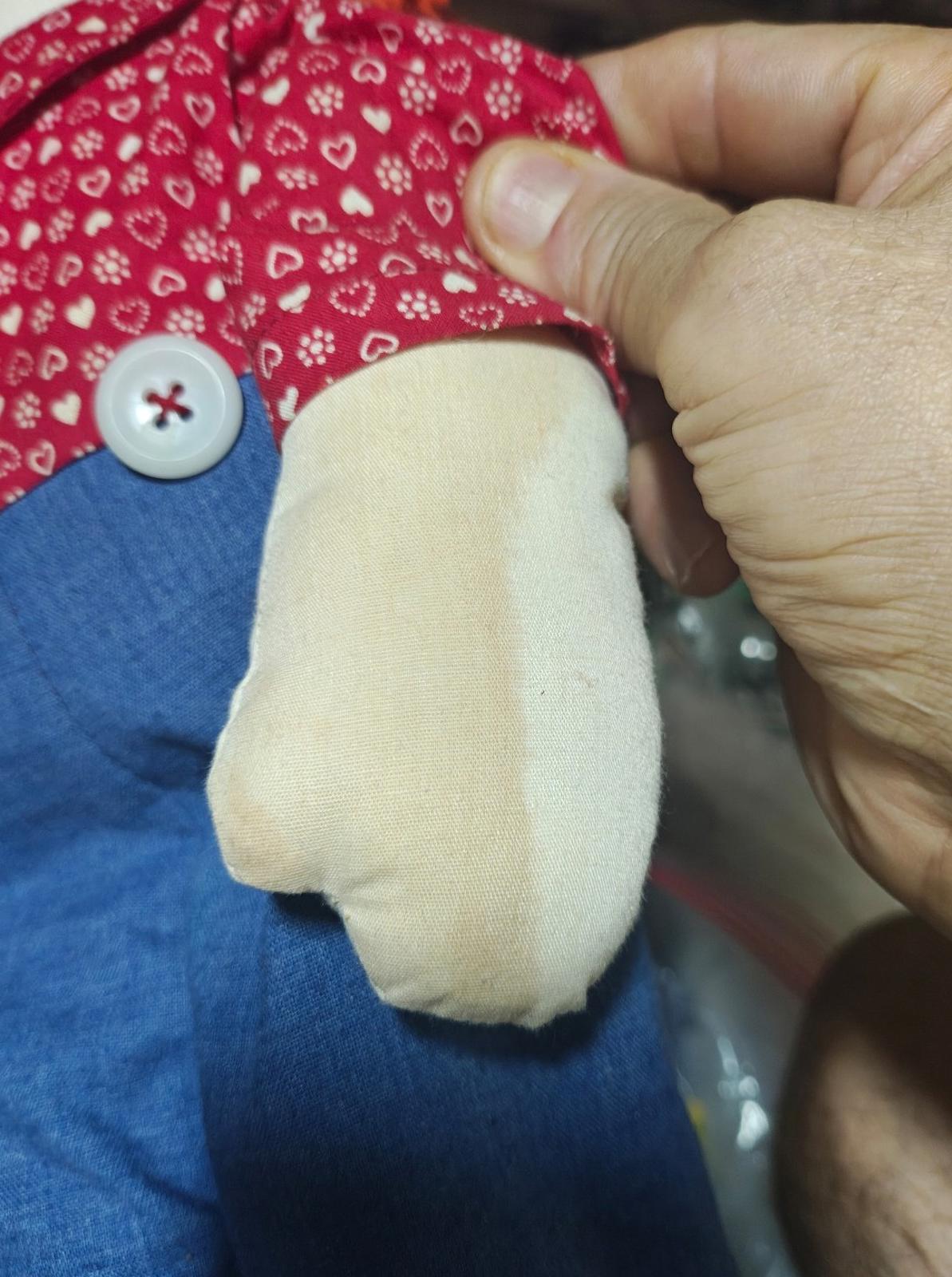 Close-up of handmade rag doll outfit: red heart-pattern shirt, blue overalls, stitched seam and button.