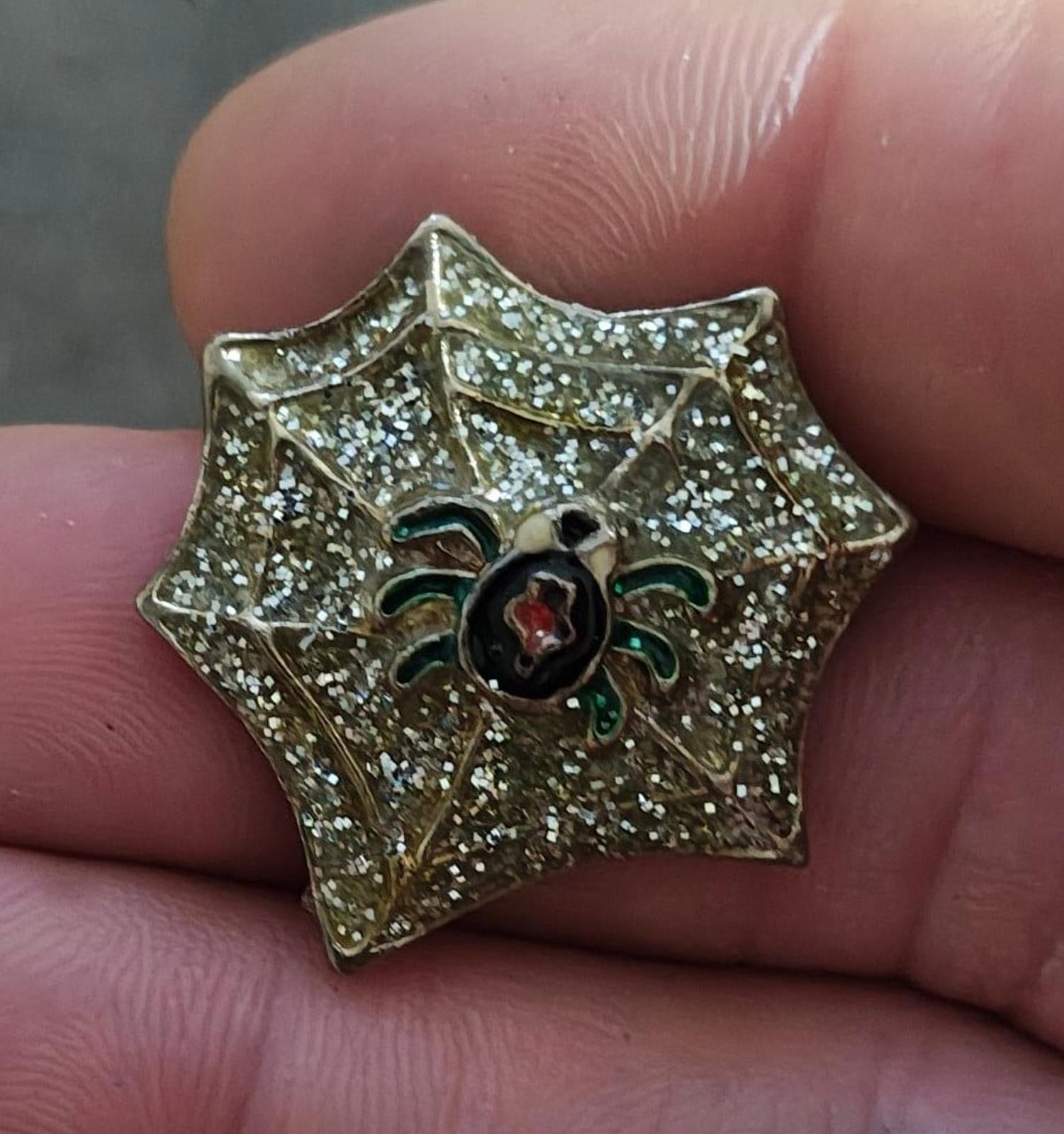 Gold spider web enamel pin with glitter sparkle, black spider body, red center, green legs