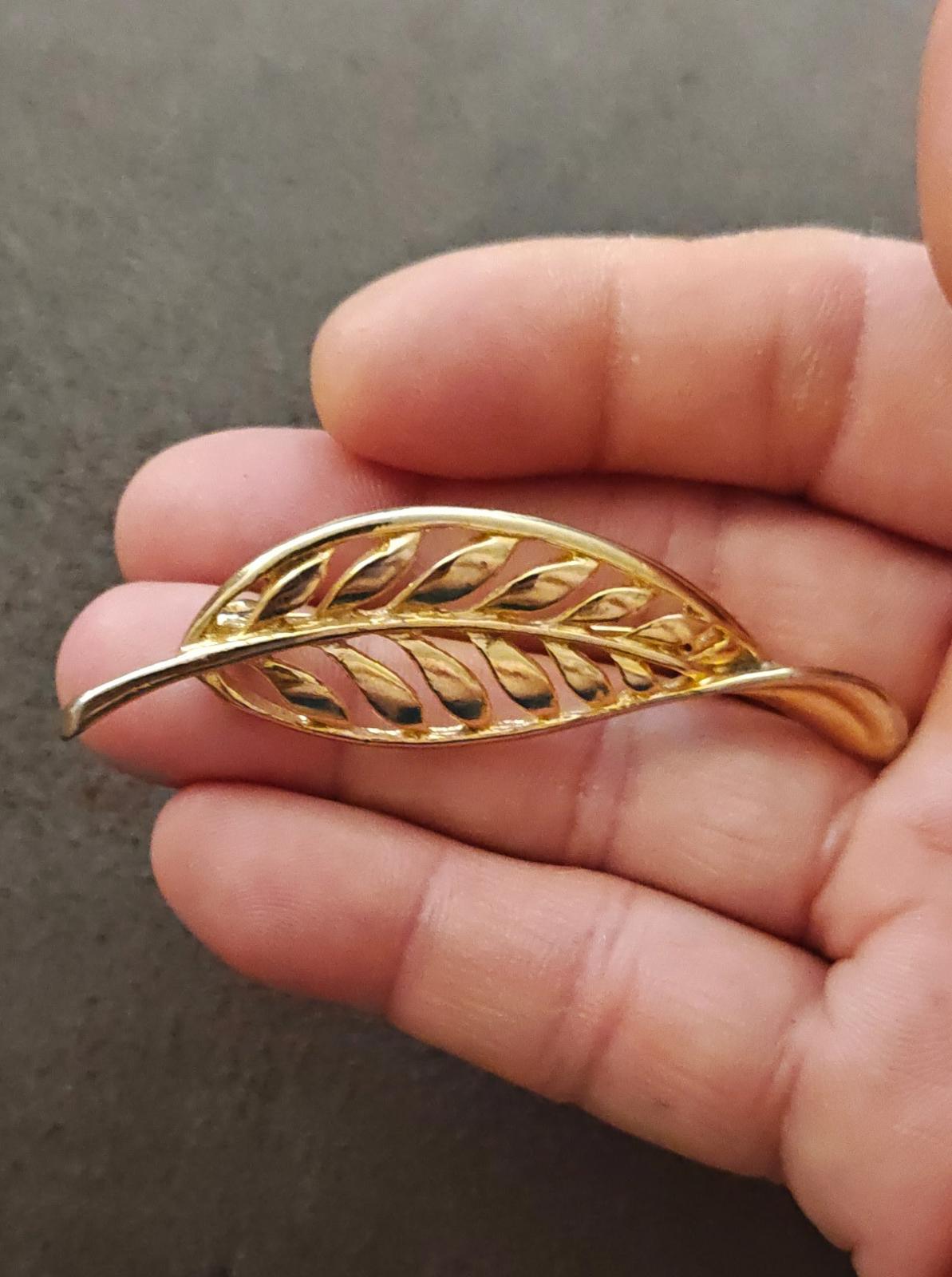 Gold tone leaf brooch with openwork filigree feather motif, close-up