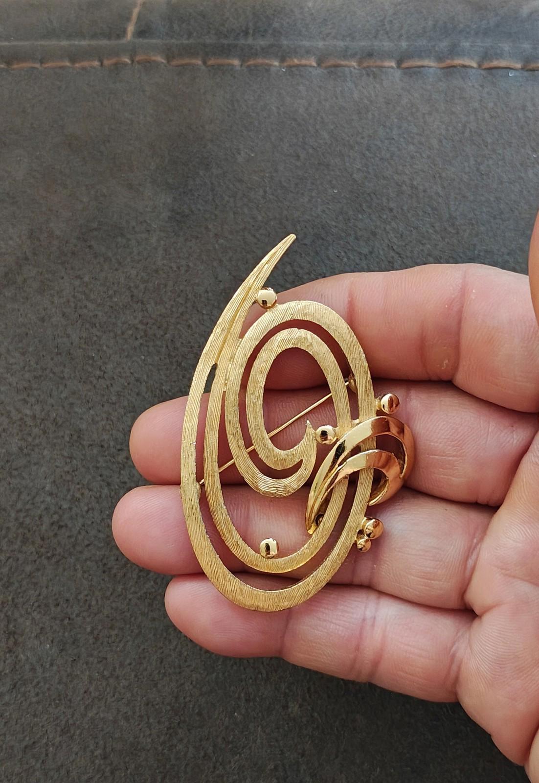 Gold tone double swirl oval brooch pin held in hand, textured metallic finish
