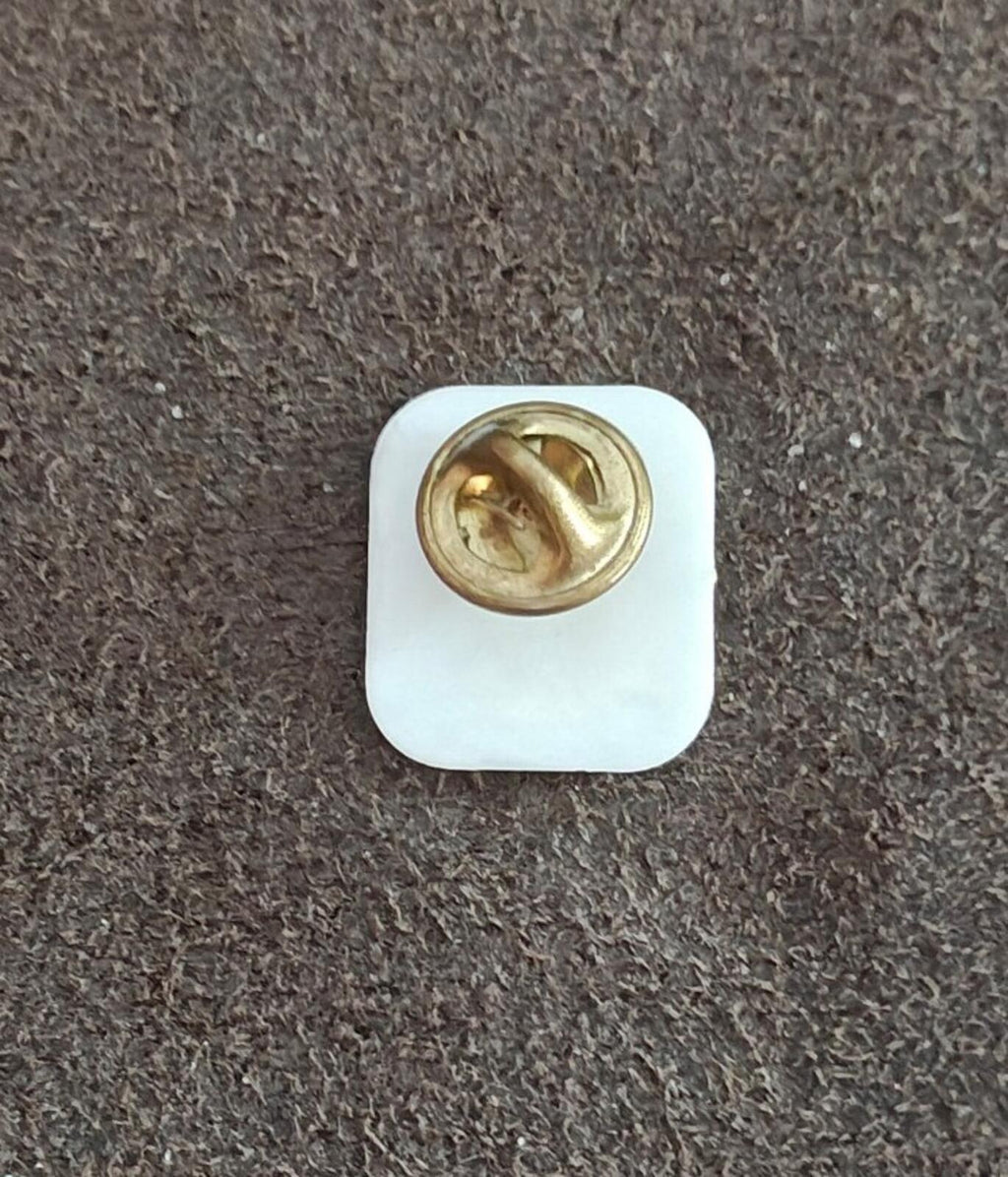 Souvenir pin back with gold metal clasp on white square plastic backing