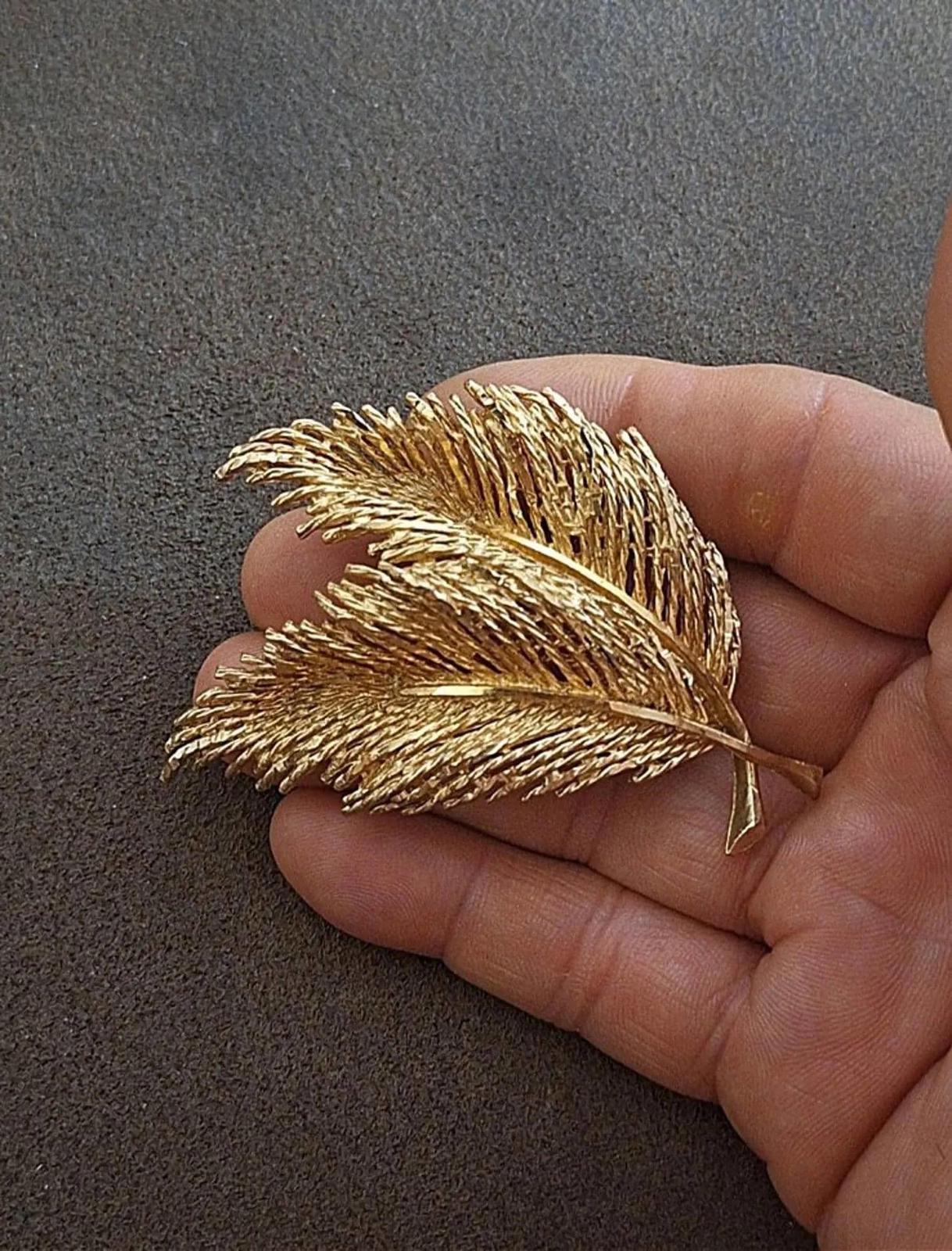 Gold-tone two-feather leaf pin brooch with small pointed leaf detail, held in hand