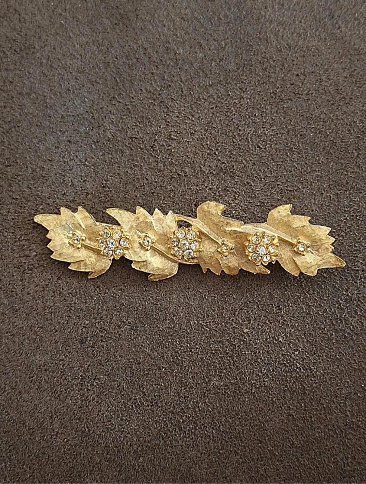 Gold tone leaf rhinestone brooch pin laid flat, row of sparkle centers