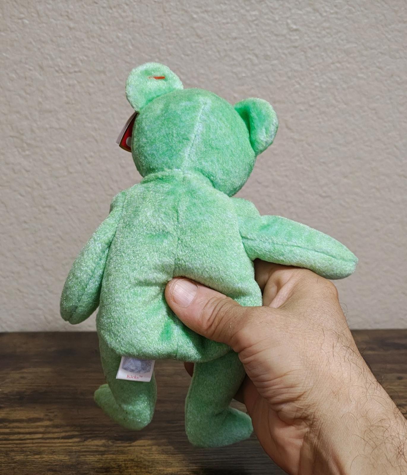 Green teddy bear plush, back view with white hang tag; arms extended.