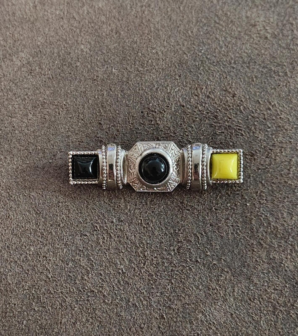 Silver-tone cabochon bar brooch featuring dark center stone, black square, and yellow square