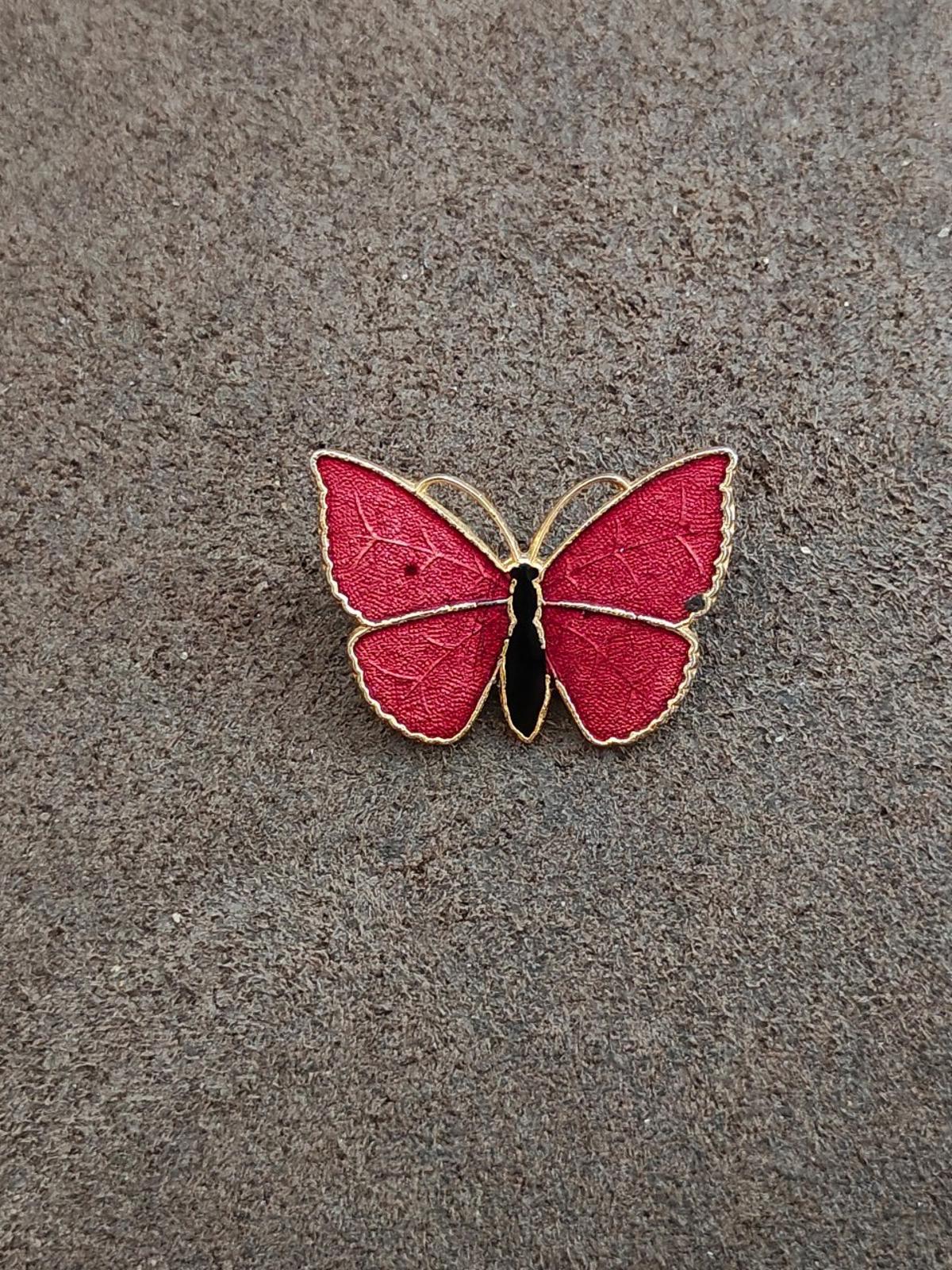 Red butterfly enamel brooch with gold-tone outline and black body, small on textured surface.