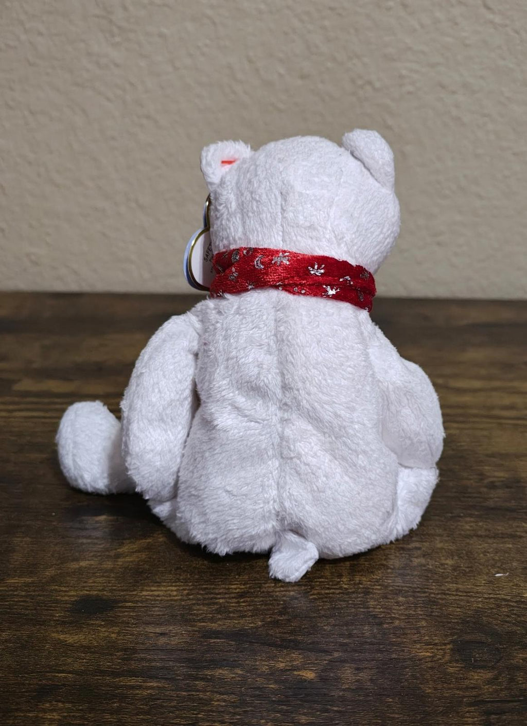 White bear plush from behind with red scarf and metal ring