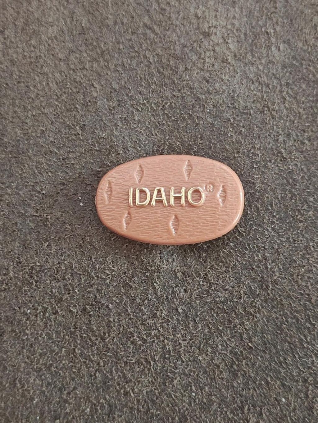 Brown plastic Idaho potato pin, small embossed “IDAHO” text and arrow pattern