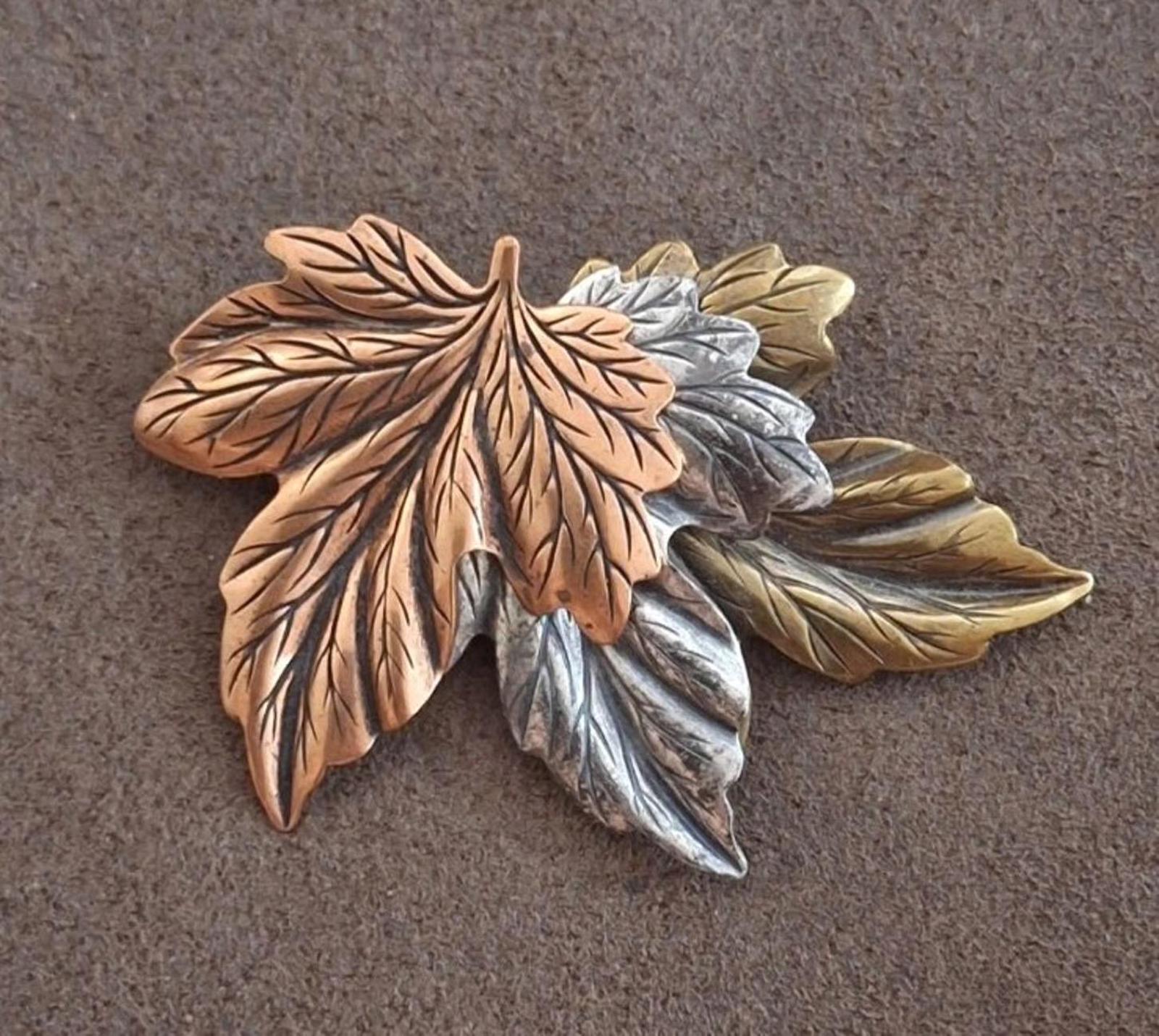 Layered leaf pin brooch with brown, gold, silver, and green-toned leaves on fabric