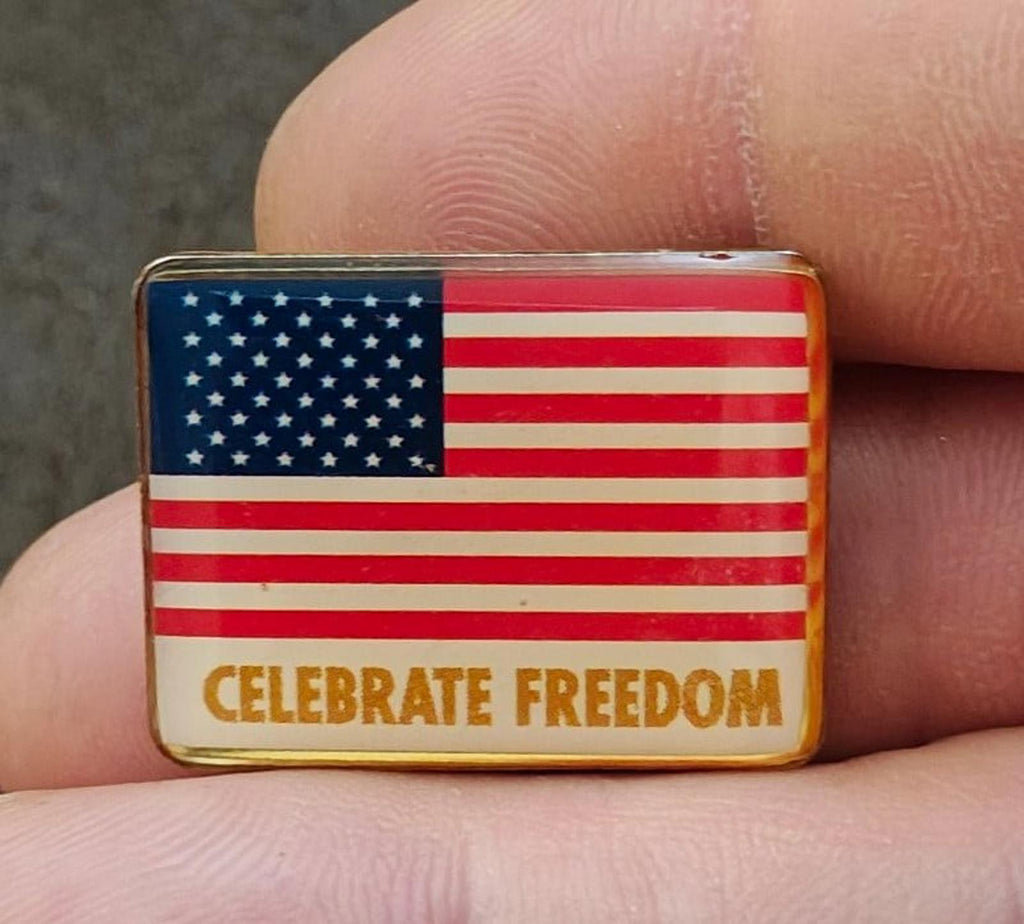 Gold-tone flag pin close-up showing “CELEBRATE FREEDOM” lettering