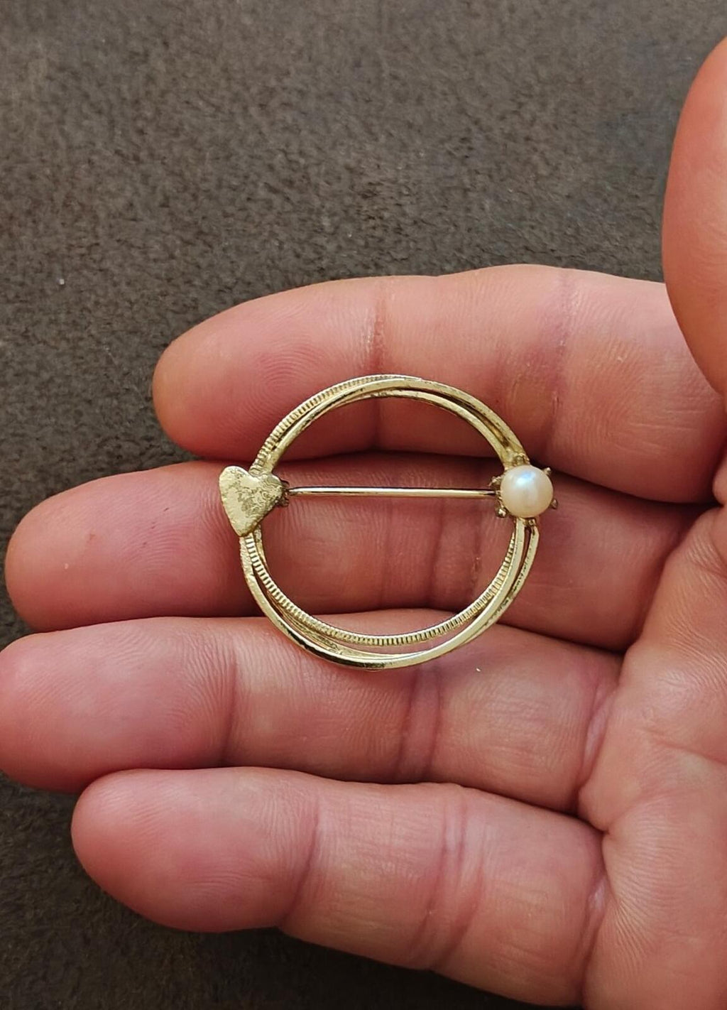 Gold-tone circle brooch with textured rim, heart-shaped detail, and pearl bead