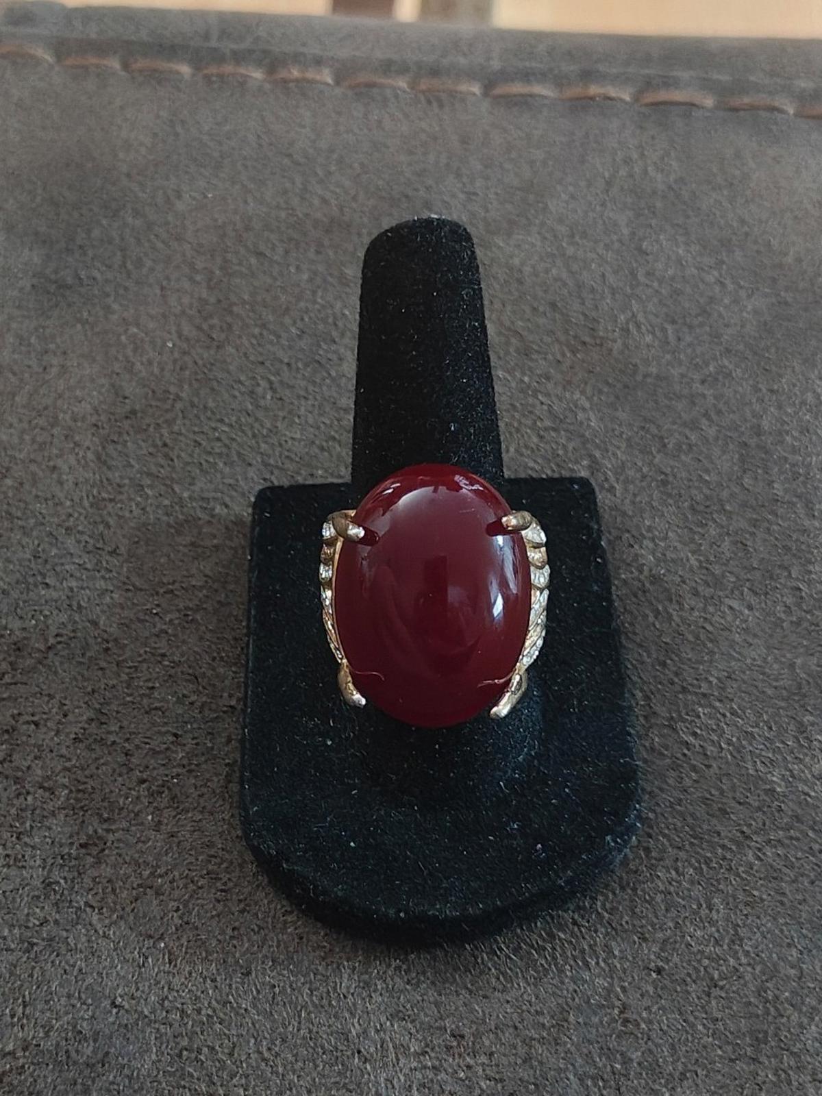 Red oval faux stone ring on black stand with gold-tone prongs and rhinestone accents
