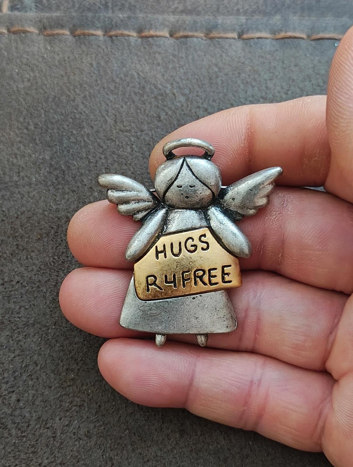 Silver winged angel brooch with tan sign reading HUGS R4FREE