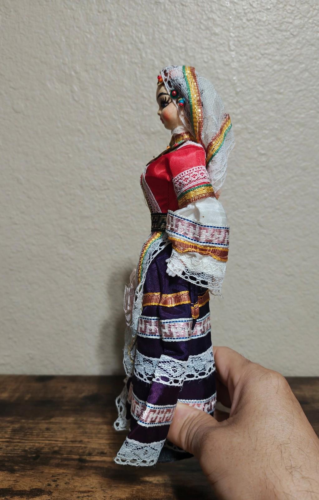 Female folk doll side view with white lace sleeves, red bodice, and patterned skirt
