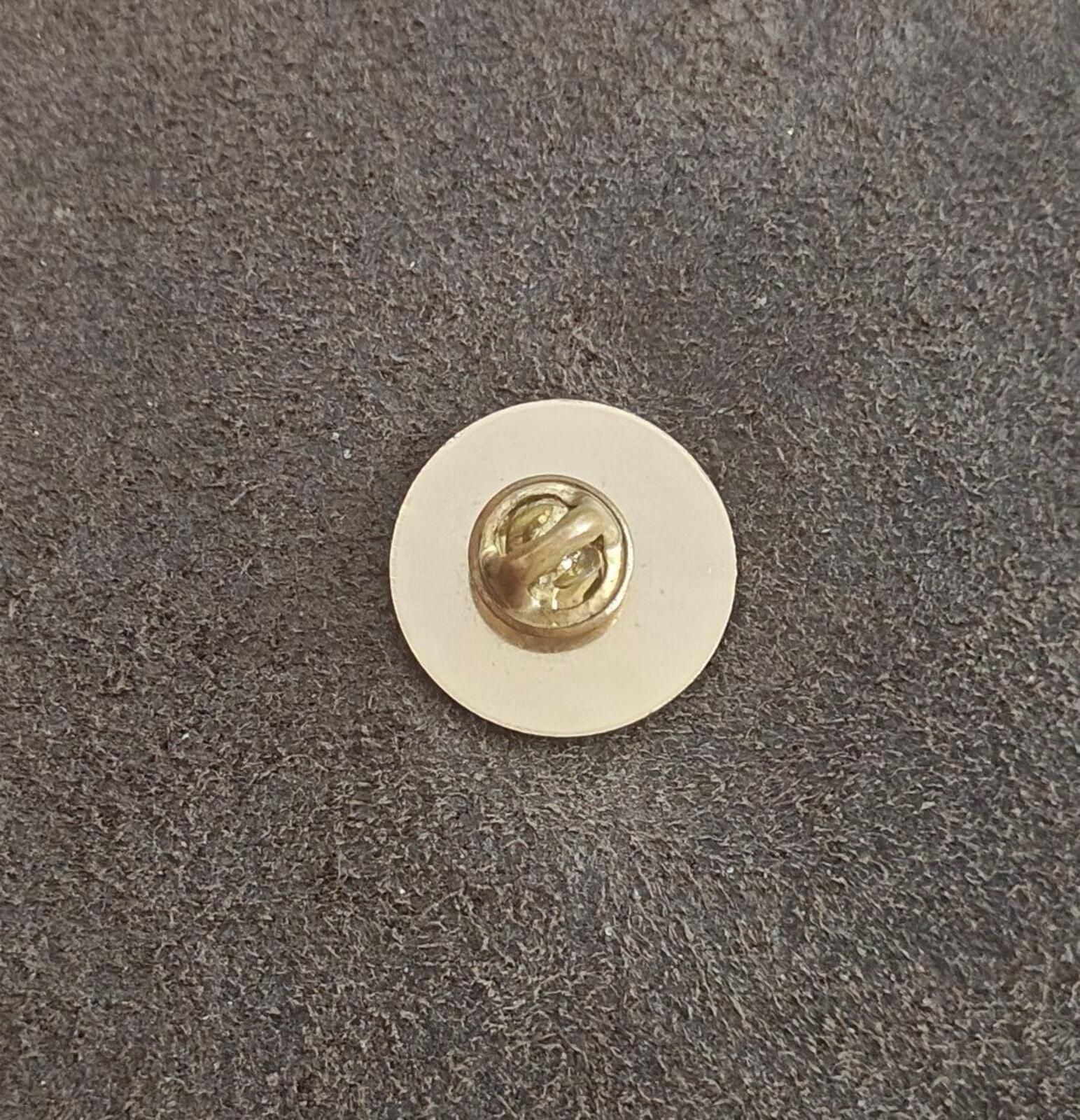 Gold-tone dartboard pin back with metal post and secure clasp on a circular backing.
