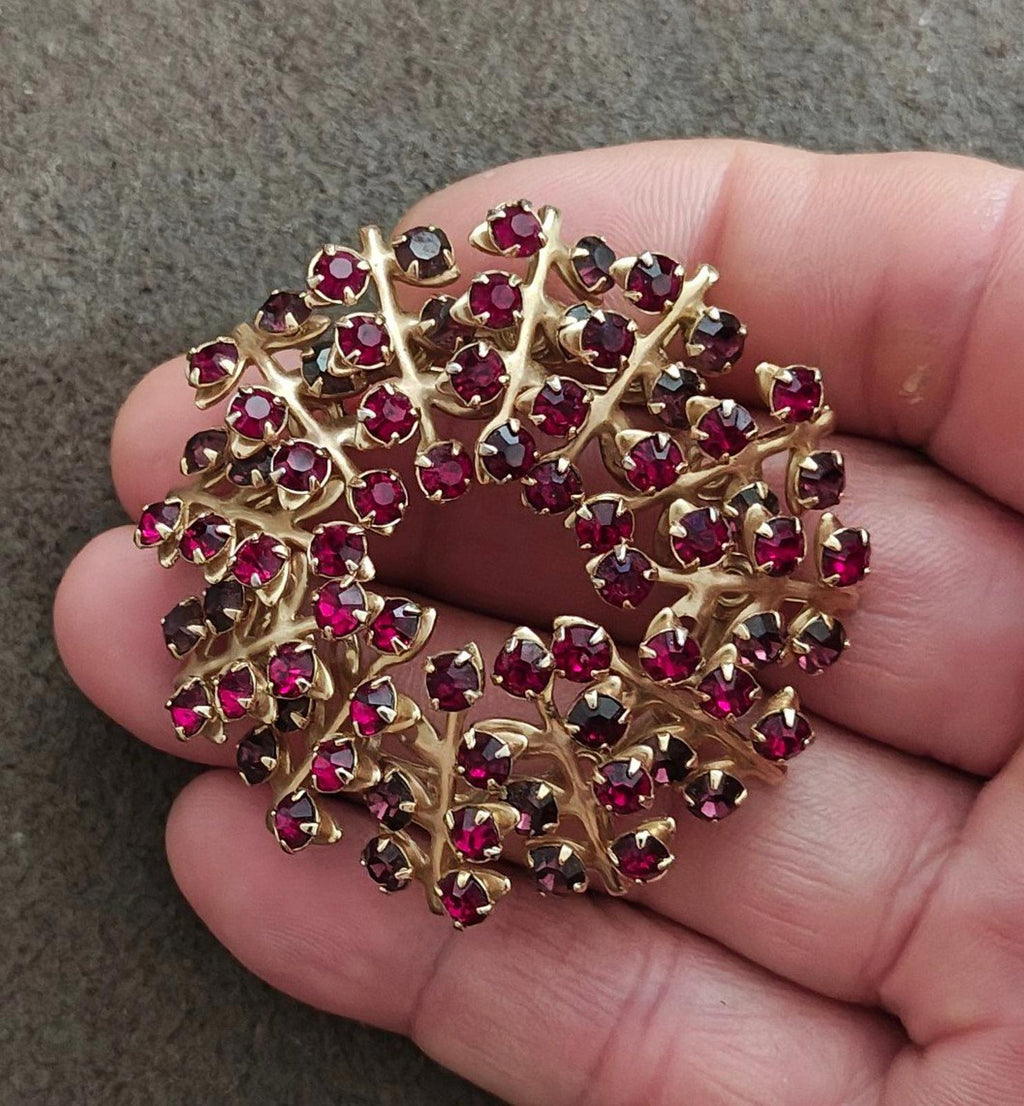 Gold-tone maroon rhinestone brooch pin held in hand, ornate wreath style