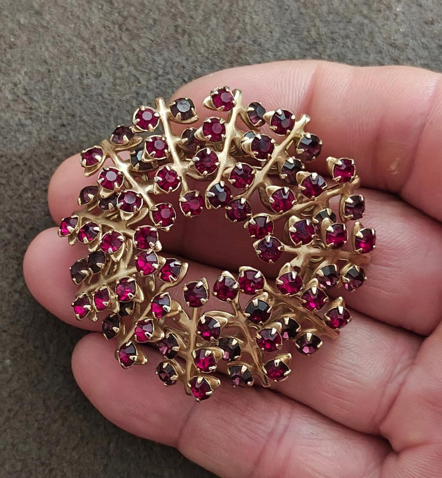 Gold-tone maroon rhinestone brooch pin held in hand, ornate wreath style