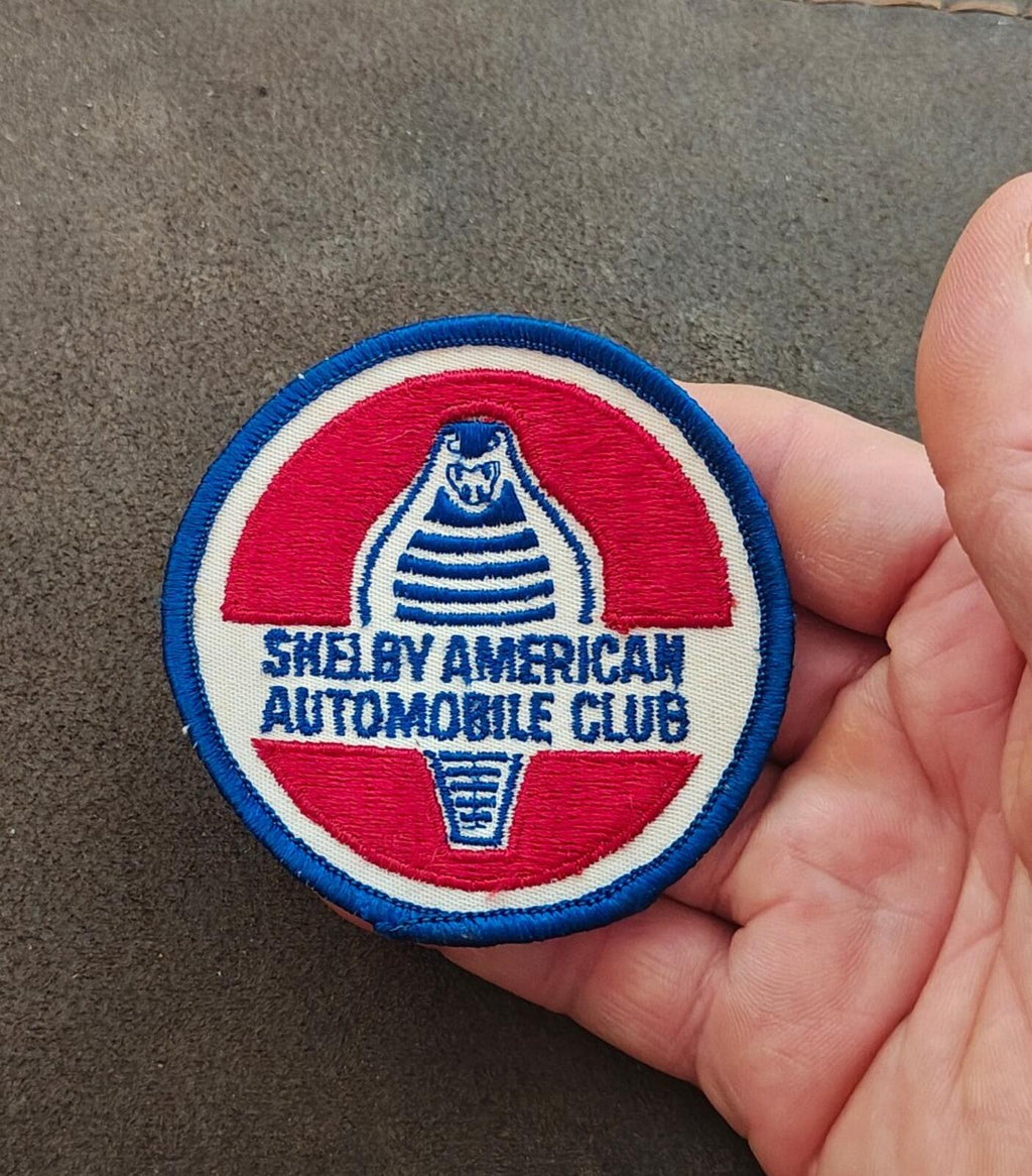 Round Shelby American Automobile Club patch held in hand; blue border and red-white field