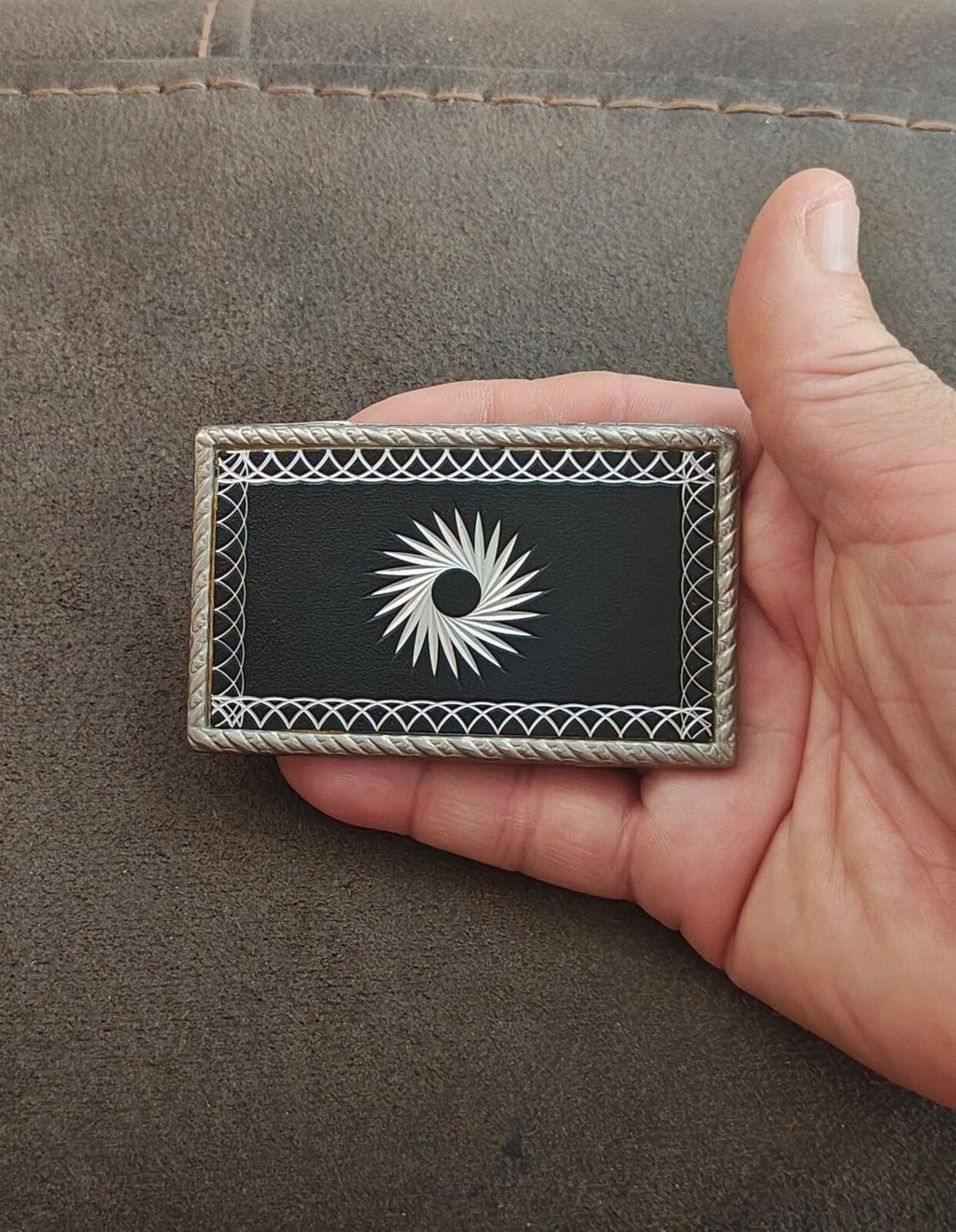 Western belt buckle in hand, silver starburst etched on black center plate