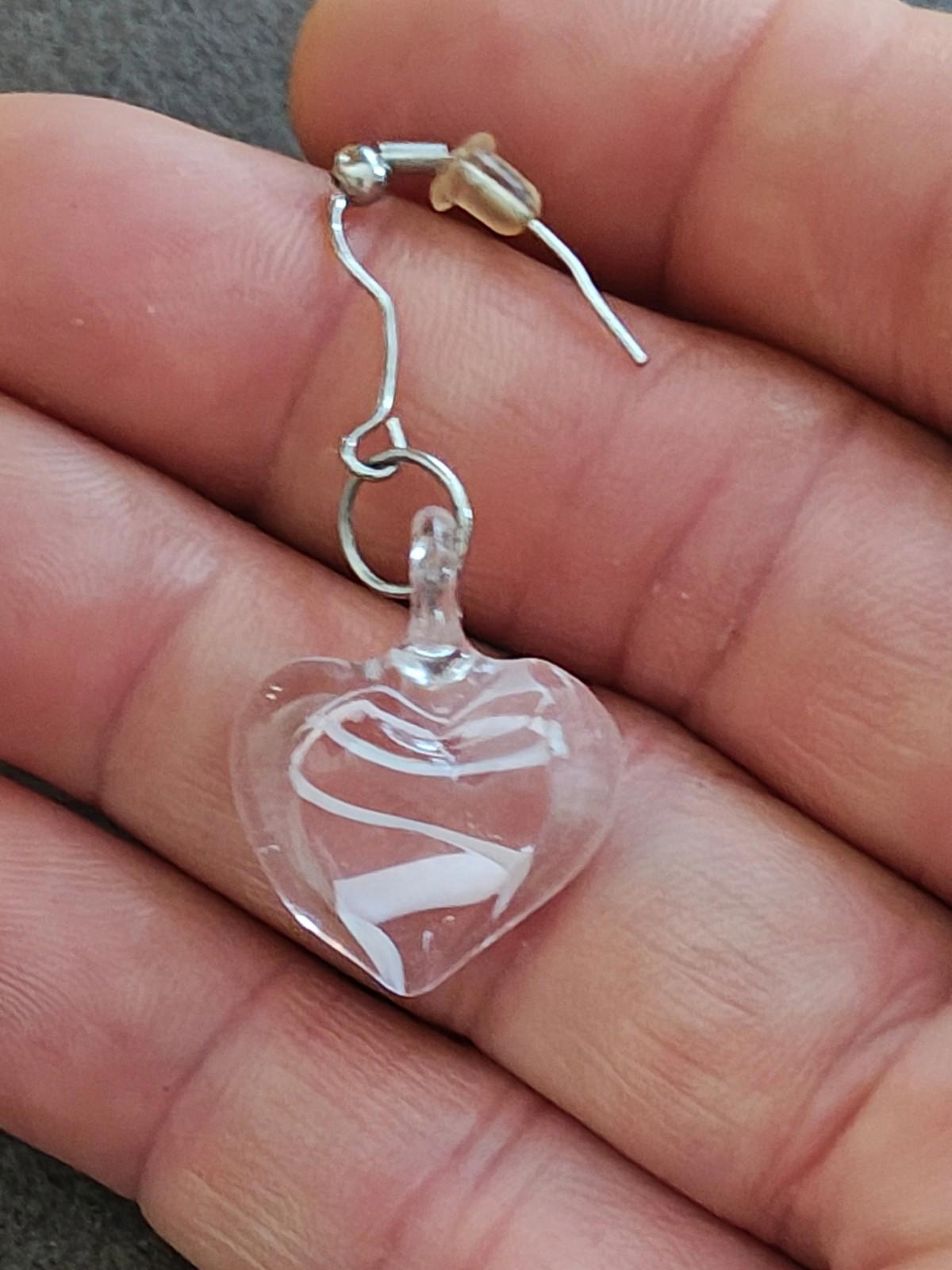 Close-up of heart-shaped clear glass earring with swirl pattern on silver hook.