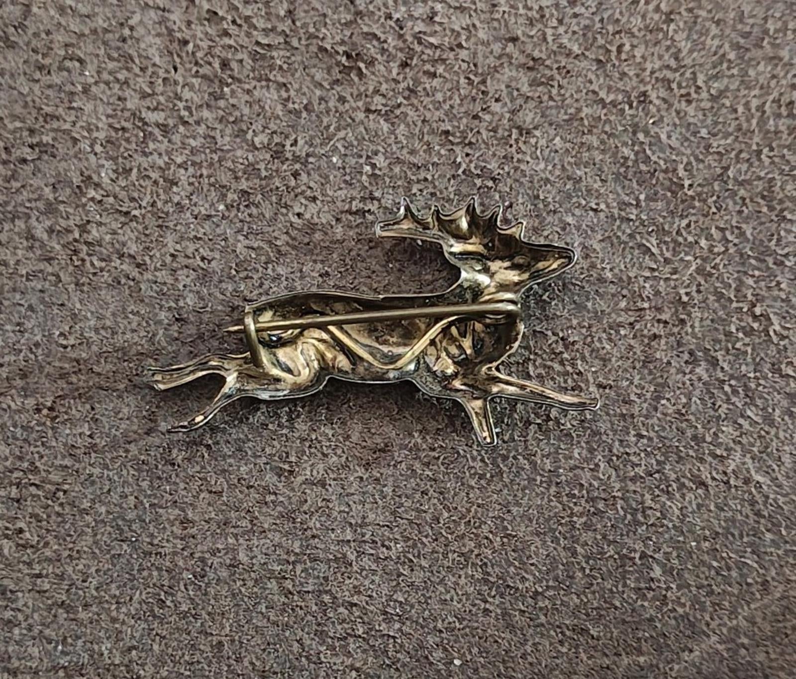 Brass deer figurine with arched antlers, running pose on textured gray surface