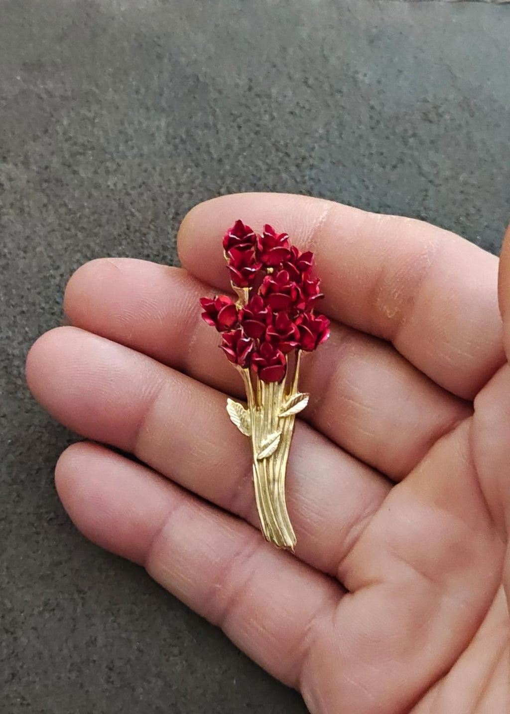 Gold tone rose bouquet brooch with red roses and gold leaf accents, held in fingers