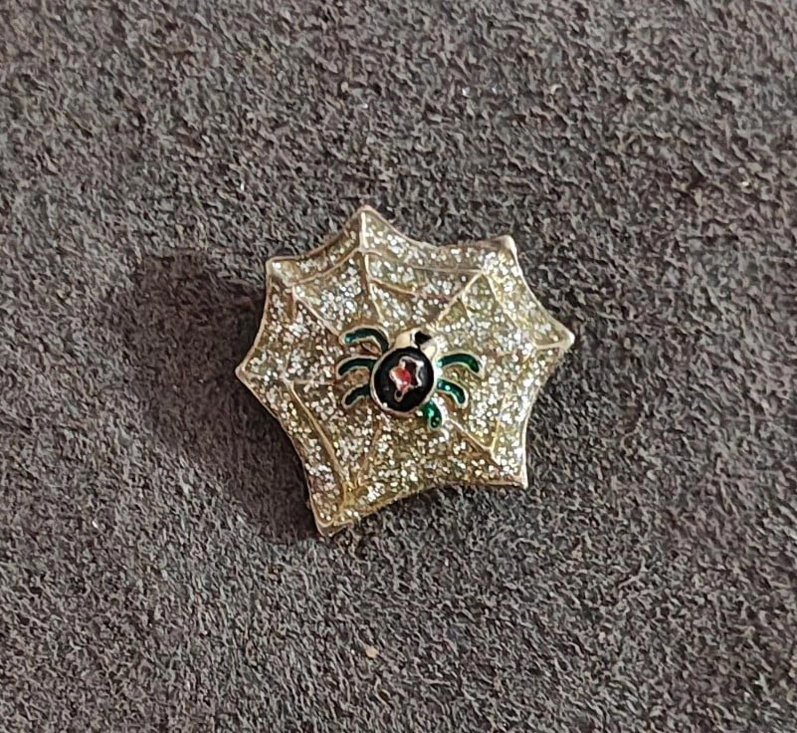 Gold glitter spider web enamel pin, black spider with red oval center and green leg details