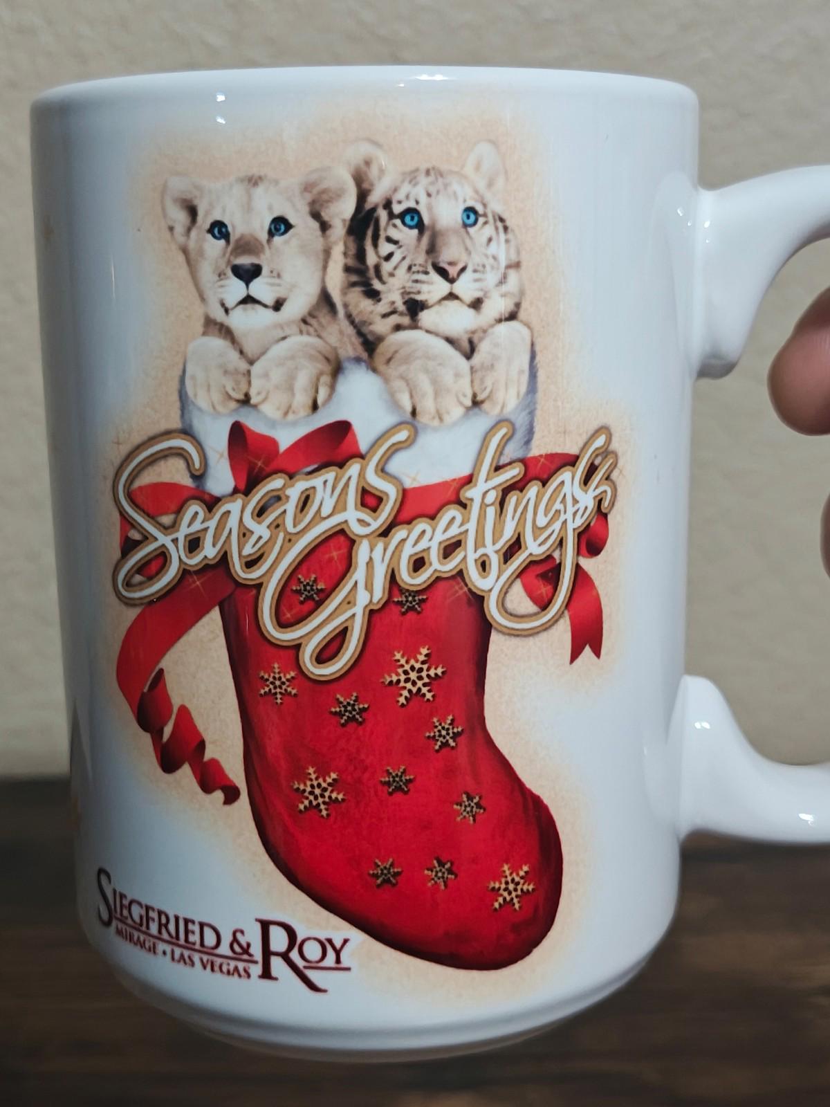 White porcelain mug close-up showing two big cats and a red “Seasons Greetings” stocking design