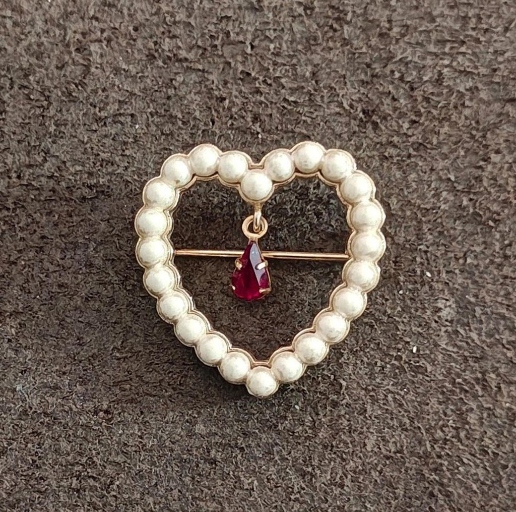 Heart-shaped brooch with white faux pearls and a red teardrop rhinestone hanging centerpiece