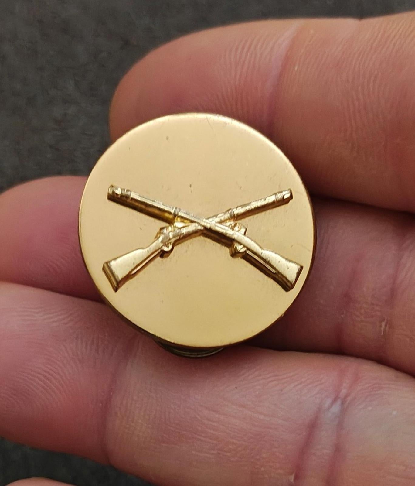 Gold circular brass pin with crossed rifles emblem, front view