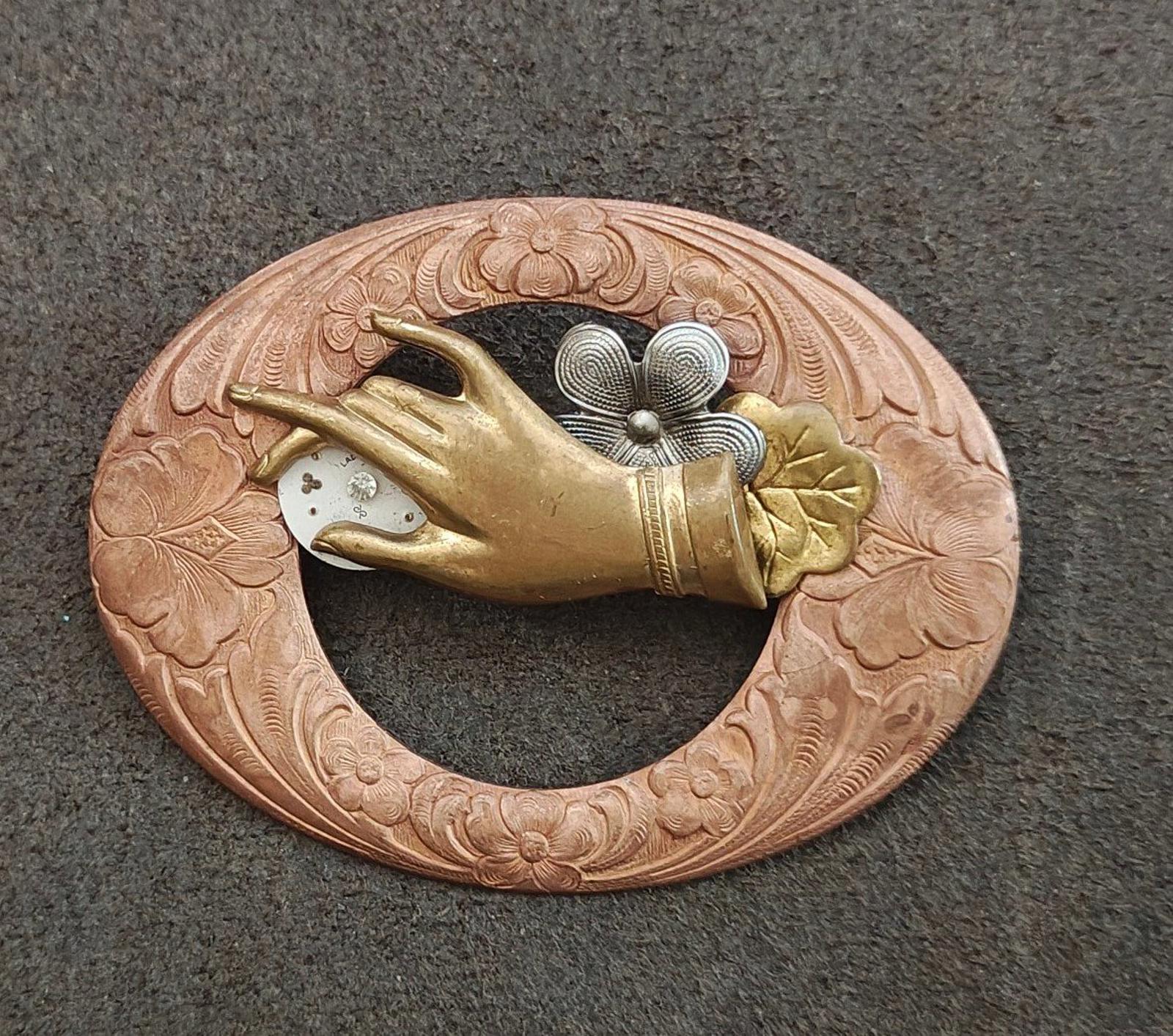 Bronze circular brooch with ornate engraving, gold bird, and textured gray flower