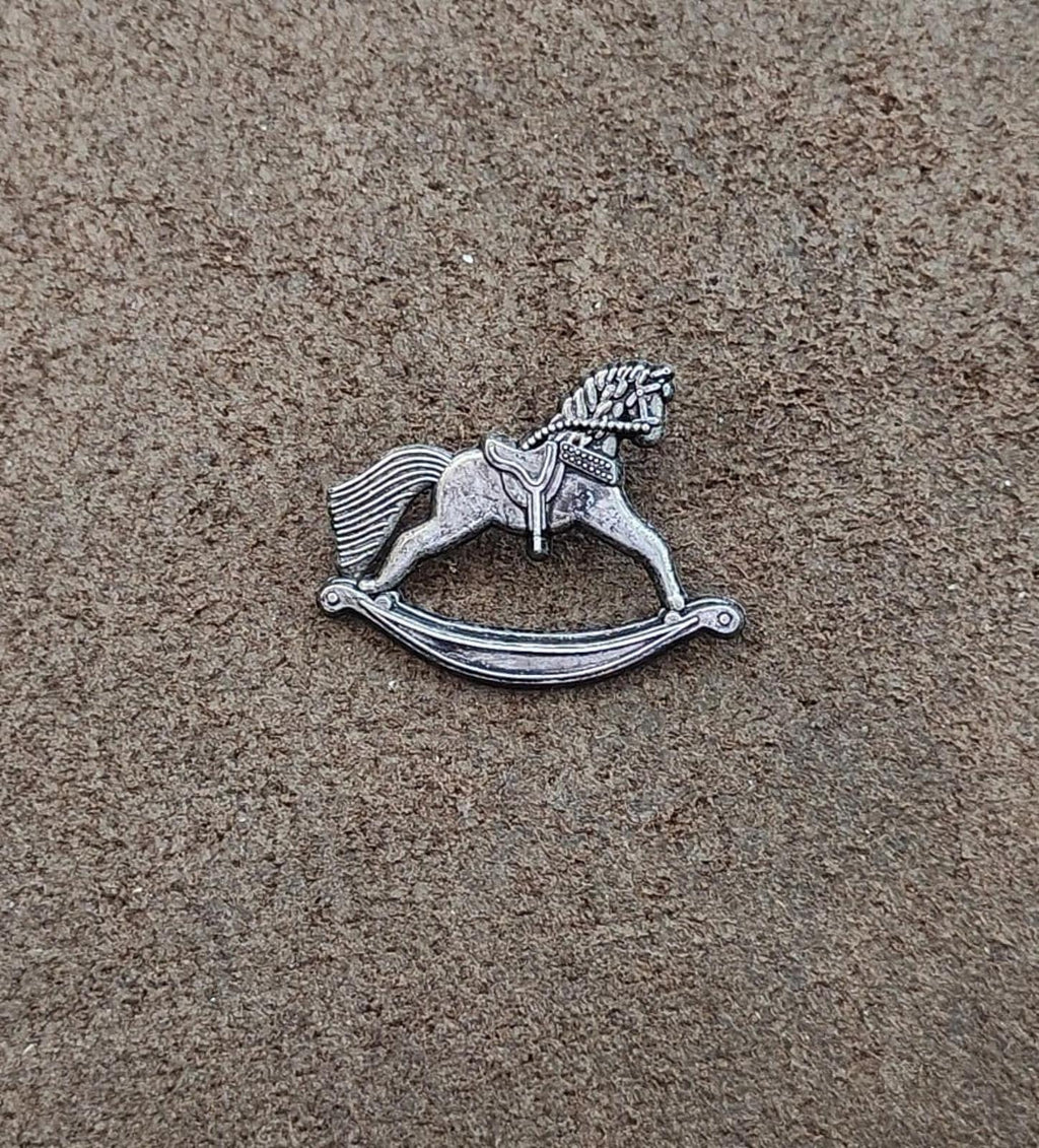 Silver-toned pewter rocking horse pin on the surface, small detailed rocking figure.