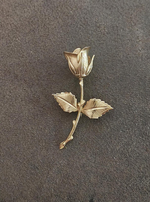 Gold-tone rose brooch with textured petals and three layered leaves on pin stem