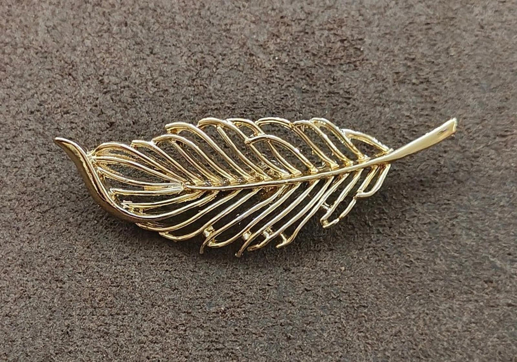 Gold-tone openwork leaf brooch on textured surface with long pointed tips