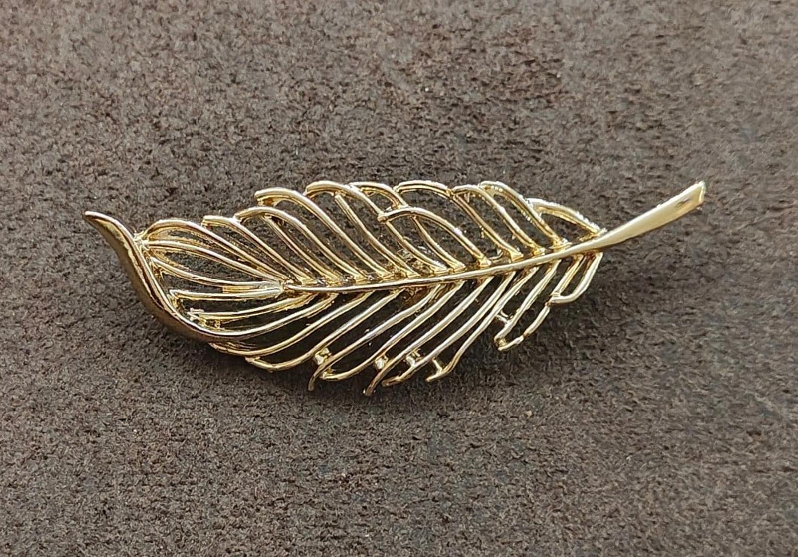 Gold-tone openwork leaf brooch on textured surface with long pointed tips