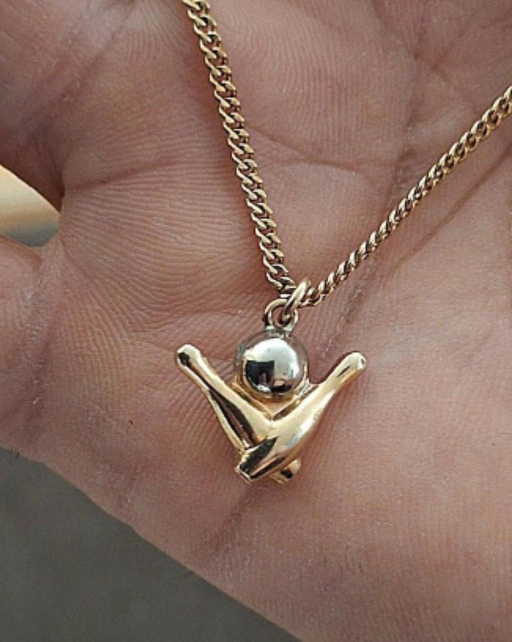 Gold-tone bowling pin charm pendant on chain, shown resting on an open hand.