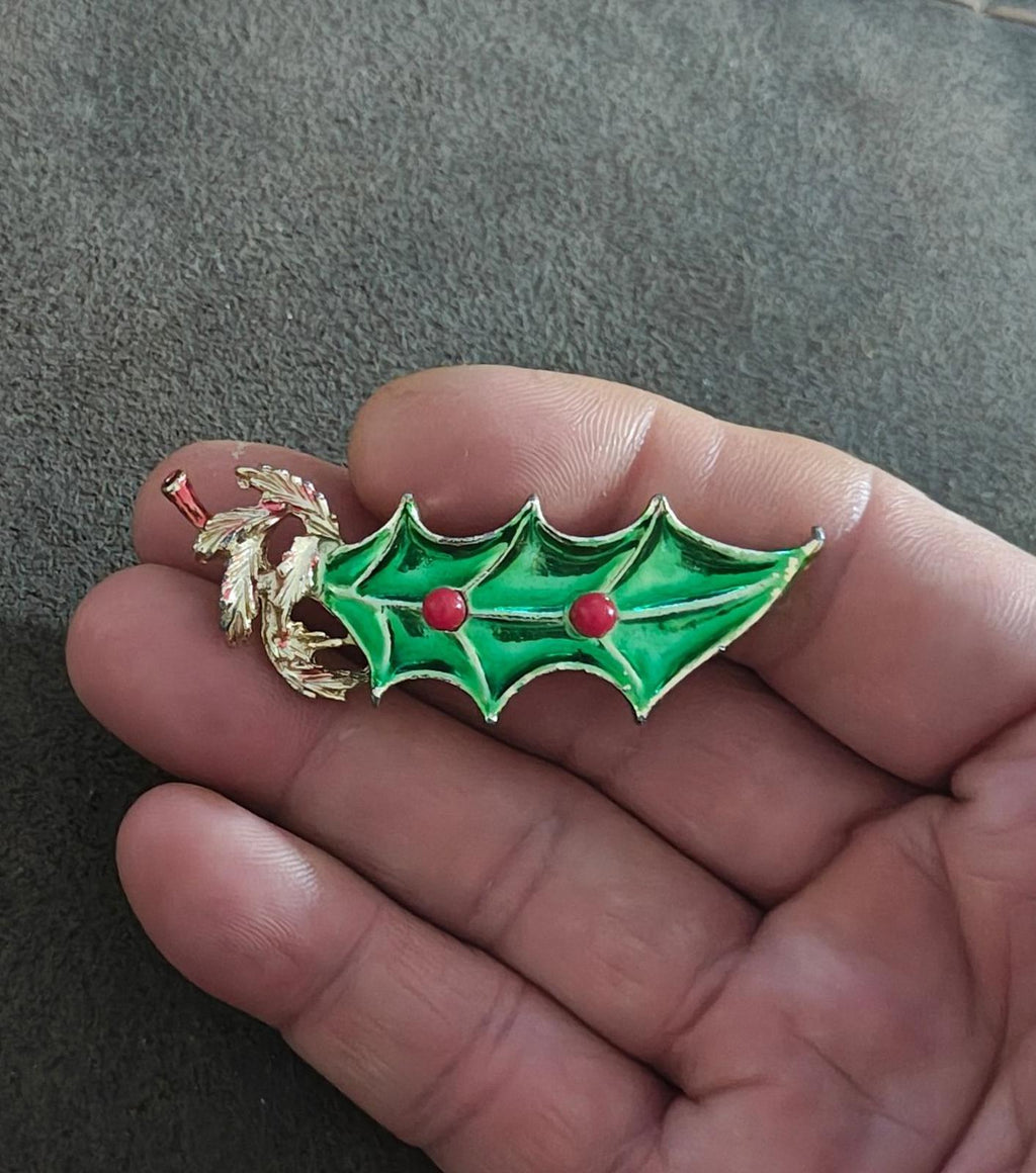 Green holly Christmas brooch with gold tone metal edges and red berry accents.