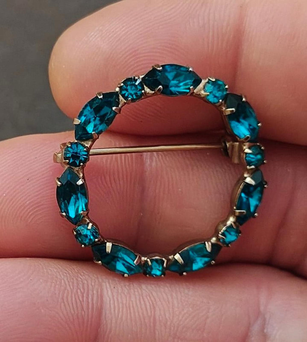 Aqua blue rhinestone circular brooch pin with gold-tone bar clasp, close-up view
