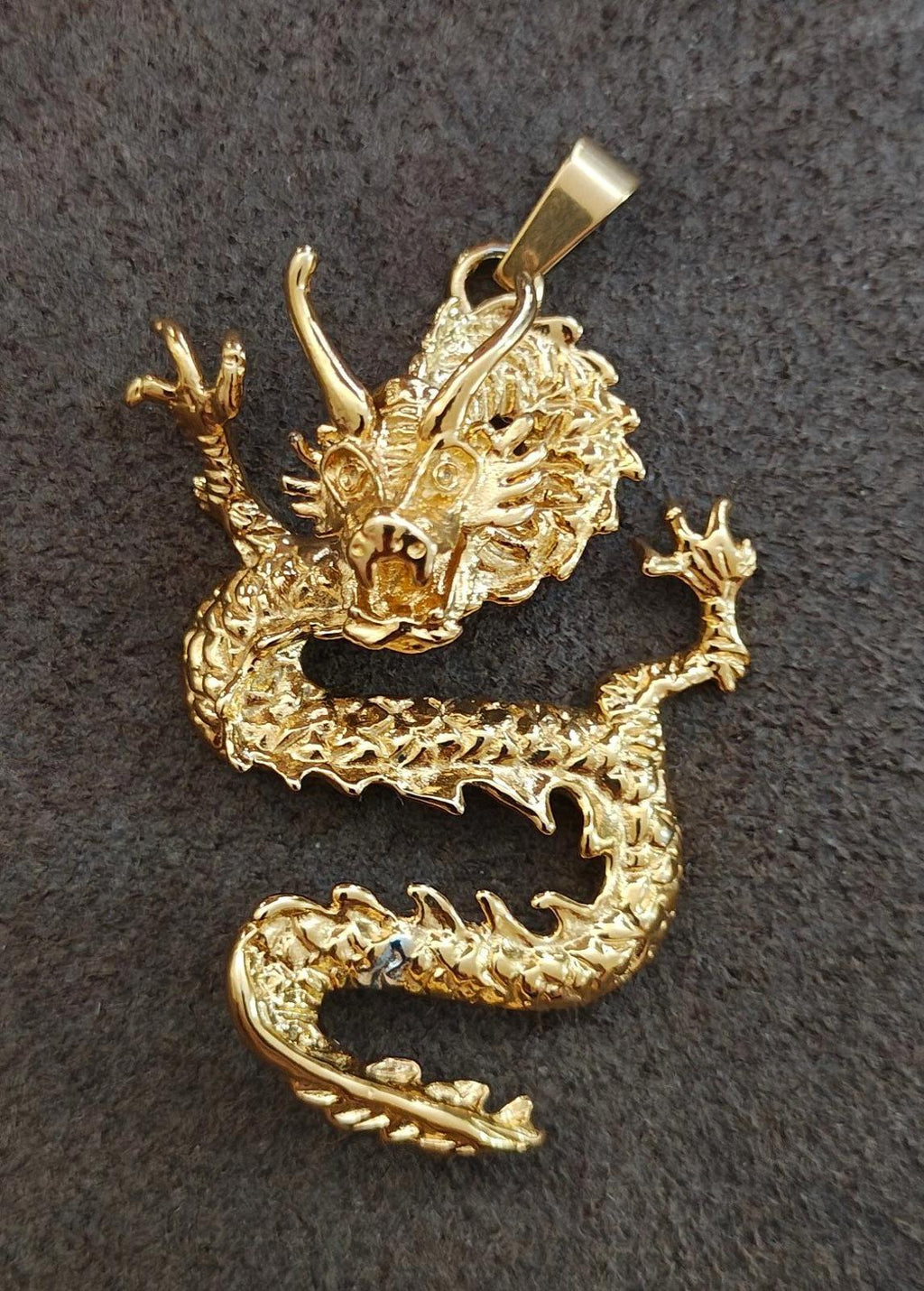 Gold-tone dragon pendant lying flat, claws raised and bail loop at top