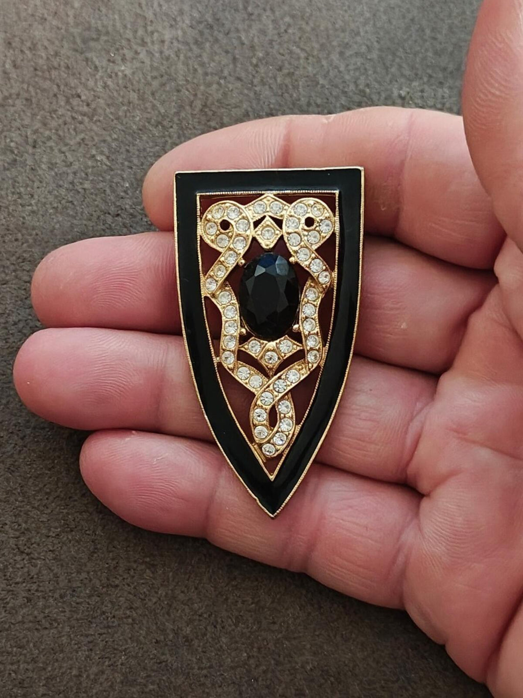 Gold tone shield brooch featuring a dark teardrop stone and clear rhinestone frame
