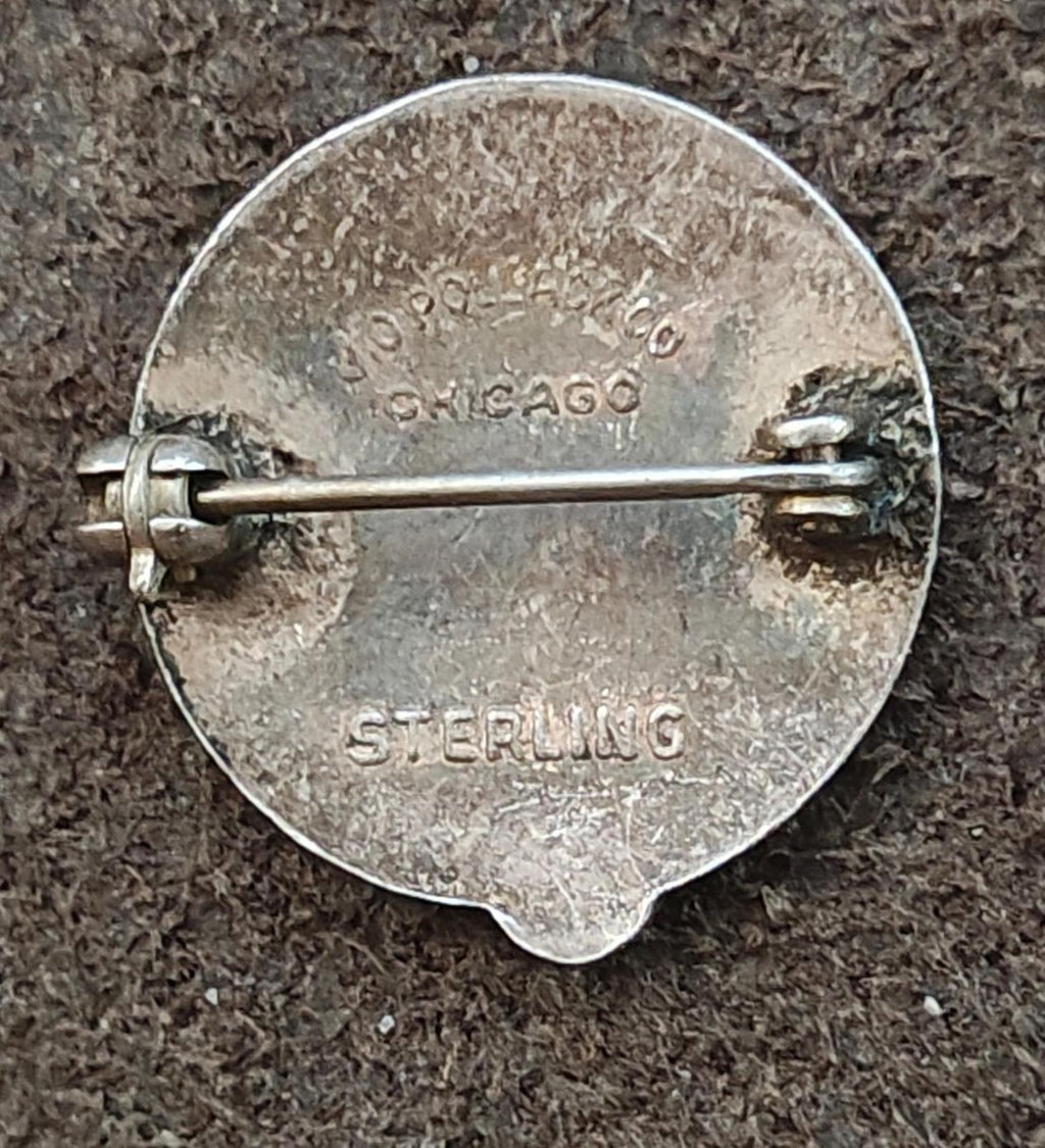 Silver pin back with stamped maker mark and Sterling text near the safety bar