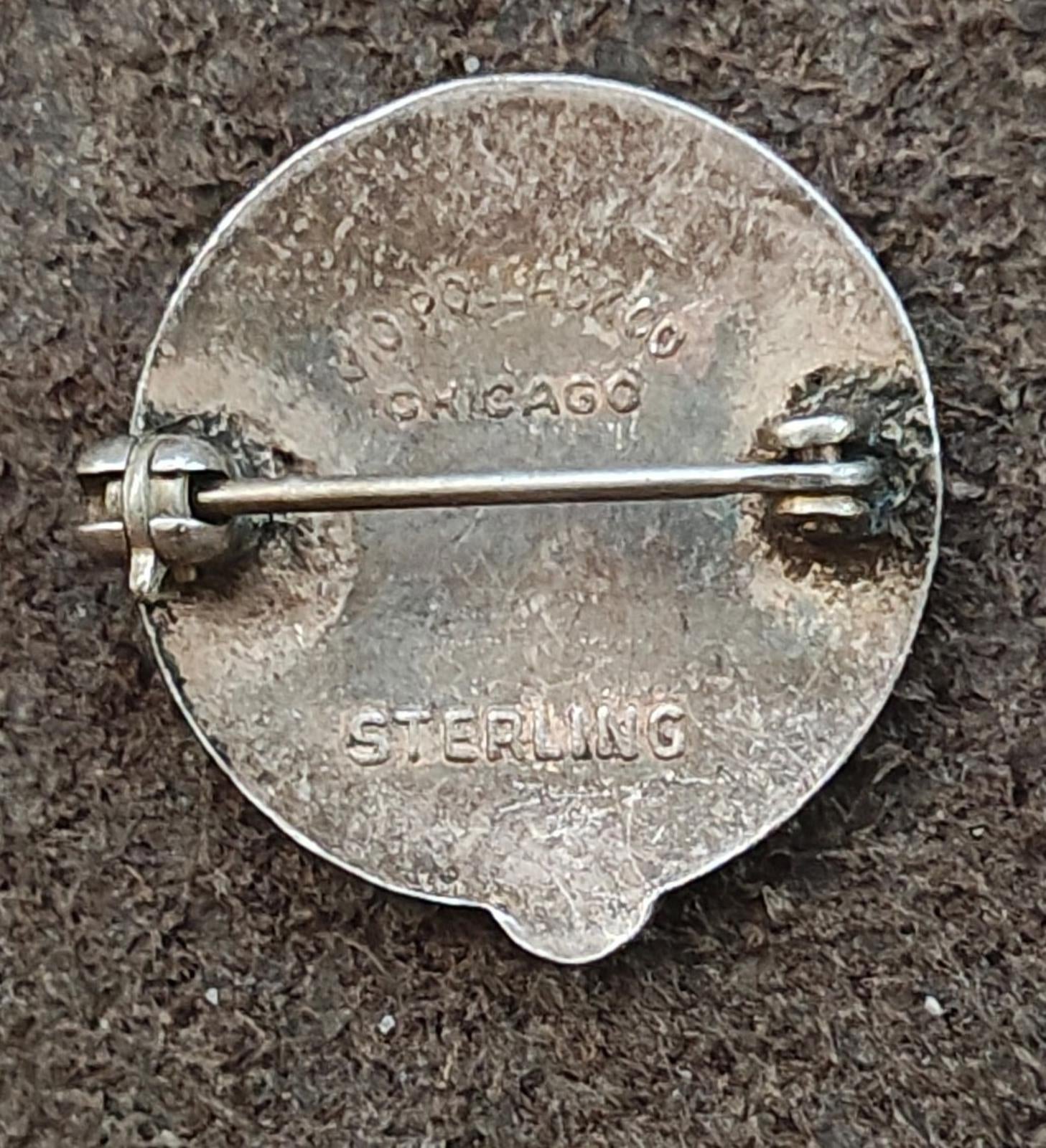 Silver pin back with stamped maker mark and Sterling text near the safety bar