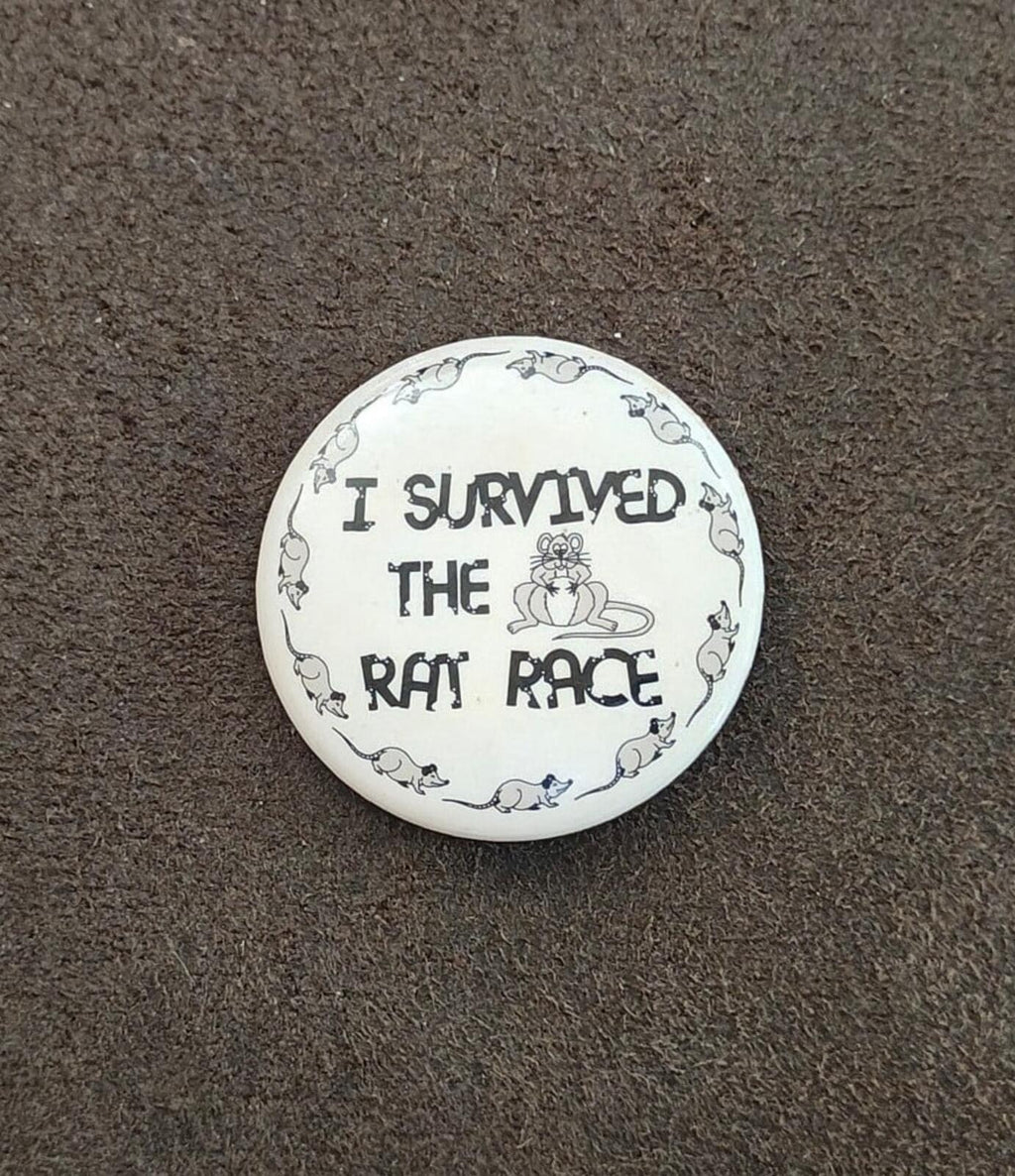 White novelty pinback button featuring “I survived the rat race” and a rat border