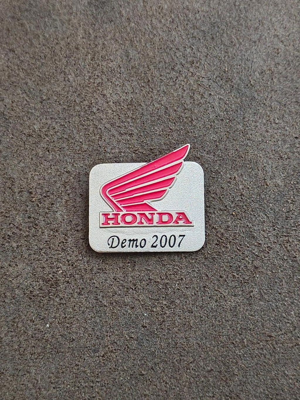 Silver-tone Honda Demo 2007 enamel pin on gray surface with red wings and HONDA