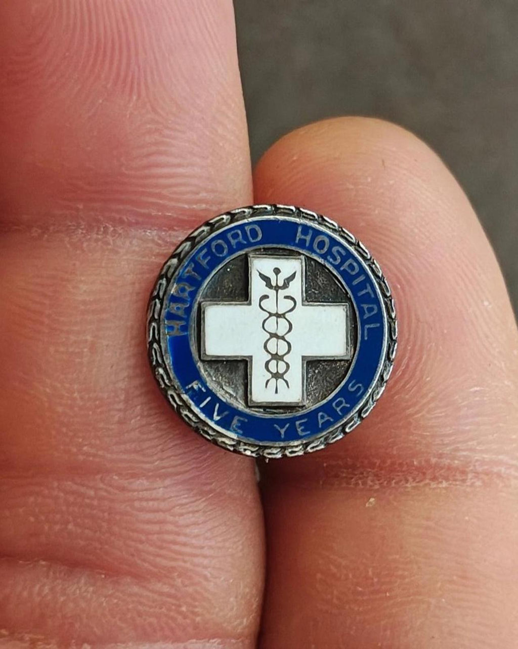 Small round enamel pin: blue ring with hospital text, white cross, caduceus, silver edge